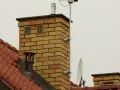 Dwa kratkowane otwory wentylacyjne na ceglanym kominie, zapewniające odpowietrzenie kanału sanitarnego.