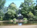 Ein ruhiger blauer See in Dorsten, umgeben von üppigem Grün. Eine kleine Holzbrücke überspannt das Wasser, während Enten friedlich schwimmen.
