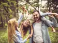 Glückliche Familie im Park. Vater trägt Tochter auf den Schultern, Mutter hält ihre Hände. Kein Anzeichen von Einzelkind-Syndrom, nur pure Freude.