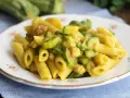 Piatto di pasta penne con zucchine a rondelle e cubetti di pancetta croccante, condita con una salsa cremosa.