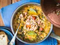 Zuppa ricca con fagioli, verdure e spezie, servita in una pentola di rame. Un piatto confortante di acqua cotta, guarnito con cipolla rossa e alloro.