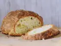 Chrupiący, złocisty bochenek soda bread, z jednym plastrem odciętym, na drewnianej desce.