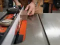 Hands guide a wooden plank along a table saw's fence, demonstrating how to use a table saw for precise cuts.