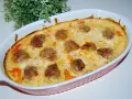 Pulpety w sosie śmietanowo-serowym, zapieczone w naczyniu, z zieloną dekoracją w tle.