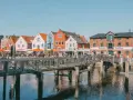 Bunte Häuser am Hafen, ein Steg führt über das Wasser. Perfekt für Ausflüge in Husum, mit Cafés und dem alten Speicher.