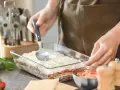 Osoba nakłada sos na warstwy makaronu i mięsa, przygotowując do pieca lasagne.