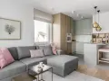 Nowoczesny salon z aneksem kuchennym: szara sofa, pastelowe poduszki, drewniane meble i marmurowa wyspa. Idealne jak urządzić mały salon z aneksem.