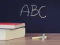 Libri e gessetti su un tavolo di legno, con la scritta "ABC" su una lavagna scura. Un'immagine che evoca l'inizio di nuovi percorsi di apprendimento, come i **corsi abilitanti**.