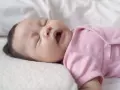 Ein süßes neugeborenes Baby in rosa Strampler niest. Die Augen sind geschlossen, der Mund leicht geöffnet.