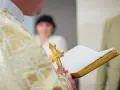 Ksiądz w złotej szacie trzyma krzyż i księgę podczas uroczystości. To ważny moment, kiedy odbywa się bierzmowanie.