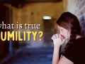 A woman with her hands clasped in prayer leans against a brick wall, contemplating "what is true HUMILITY?".