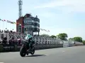 Motocyklista ściga się na wyspie Man, mijając trybuny pełne widzów i wieżę kontrolną.