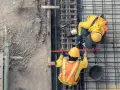 Dwóch budowlańców w żółtych kamizelkach pracuje przy zbrojeniu. To ważny etap w budowie każdego obiektu budowlanego.