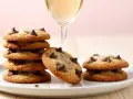 Gestapelte, goldbraune American Cookies mit Schokoladenstückchen und ein Glas Sekt.