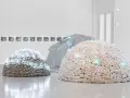 Installation d'art povera : dômes en pierres et en tissu, ornés de néons bleus, sous une structure transparente.