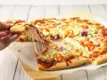 Pyszna pizza domowa z ciągnącym serem, papryką, cebulą i cukinią. Ktoś właśnie podnosi kawałek.