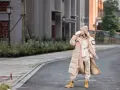 Kobieta w beżowym dresie i płaszczu pije kawę, ma na sobie żółte buty zimowe do dresów.