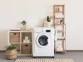 Lavadora blanca con cesta de mimbre, plantas y accesorios que se colocan en una prenda.