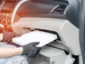 Wymiana filtra kabinowego w Audi A3 8L. Ręce w rękawiczkach wyjmują biały filtr z wnętrza schowka.