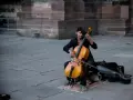 Ein Mann spielt auf einem Cello-Musikinstrument vor einer Steinfassade.