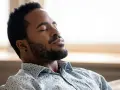 A man with closed eyes and a beard breathes deeply, finding a moment to ground himself amidst the day's chaos.