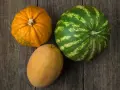 Dynia, melon i arbuz leżą na drewnianym blacie.