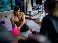 Man med rosa boll på gymmatta, tränare med clipboard. De följer sitt gymprogram.
