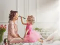 Mała dziewczynka w różowej sukience i z wałkami na włosach maluje swoją chrzestną.