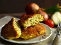 Pyszny kotlet jajeczny z ziołami, podany na talerzyku. W tle cebula i pomidorki.