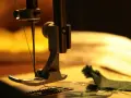 Zbliżenie na maszynę do szycia, gdzie igła do skóry z zieloną nicią przygotowuje się do przeszycia ciemnozielonego materiału.