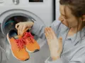 Woman holding smelly orange sneakers near an open washing machine.
