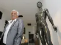 Paul Belmondo (sculpteur) pose à côté d'une de ses œuvres, une statue de bronze d'un homme nu.