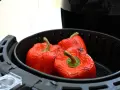 Tre peperoni rossi interi, leggermente abbrustoliti, pronti per essere cucinati nella friggitrice ad aria.