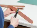 Ręce z dziurkaczem do skóry tworzą nową dziurkę w brązowym pasku.