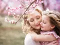 Córka tuli mamę pod kwitnącą wiśnią. Idealny obraz na Dzień Mamy.
