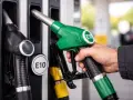 Mano che impugna una pompa di benzina verde con etichetta E10, pronta per fare rifornimento di benzina 95 ottani.