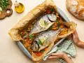 Due agoni in carpione cotti al forno con pomodorini, olive e limone, pronti per essere gustati.