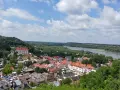 Widok na Kazimierz Dolny z górami Trzech Krzyży w tle. Rzeka Wisła, zielone wzgórza i urokliwe miasteczko z czerwonymi dachami.
