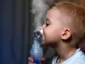 Chłopiec z maską inhalatora na twarzy, wdychający parę.