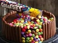 Eine einfache Geburtstagstorte für Jungs: Schokoladenkuchen, umhüllt von Schokoriegeln und bedeckt mit bunten Smarties, die aus einer aufgeschnittenen Rolle rieseln.