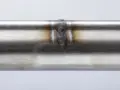 Dettaglio di una saldatura acciaio inox su un tubo metallico, con sfumature iridescenti intorno al cordone.