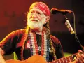 Willie Nelson mit roter Bandana und Zöpfen spielt Gitarre. Ein Mikrofon steht bereit für den Titel von Willie Nelson.