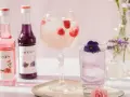 Dobre drinki przepisy: różowy i fioletowy syrop Monin, drink z malinami w kielichu, drink z fiołkiem w szklance, kwiaty w wazonach.