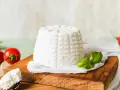 Świeża ricotta na desce, obok pomidorki i bazylia. Niskie ricotta kalorie czynią ją idealną dla dbających o linię.