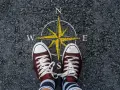 Feet stand on a compass, symbolizing the start of a journey. This image can represent the **mission creep meaning**, where initial goals expand unexpectedly.