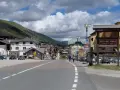 Strada verso il Passo del Tonale in moto, con case alpine e montagne sullo sfondo.