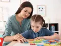 Nauczycielka wspiera dziewczynkę z niepełnosprawnością intelektualną w stopniu lekkim, układającą kolorowe puzzle.