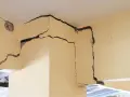 Détail d'une **micro fissure maison** sur un coin de mur en béton, révélant la structure interne.