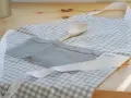 Gotowy fartuch kuchenny w kratkę, z drewnianą łyżką w kieszeni. Idealny poradnik, jak uszyć fartuch kuchenny.