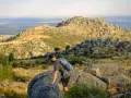 Un excursionista con mochila asciende por un terreno rocoso en la ruta Las Machotas, con un paisaje montañoso y un valle al fondo.